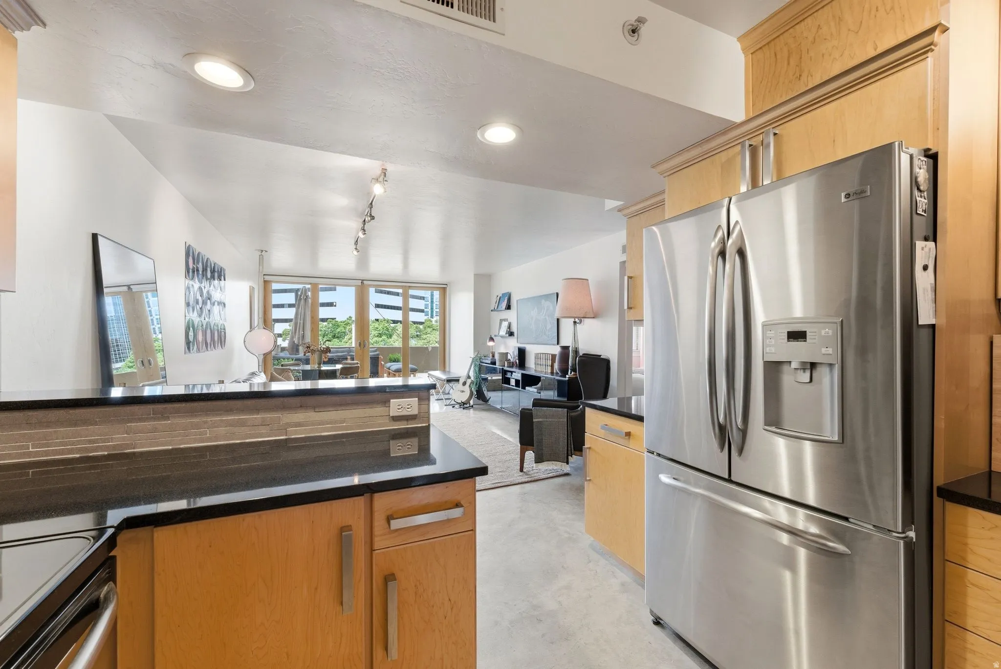 Modern kitchen featuring stainless steel appliances, light wood cabinetry, and dark countertops