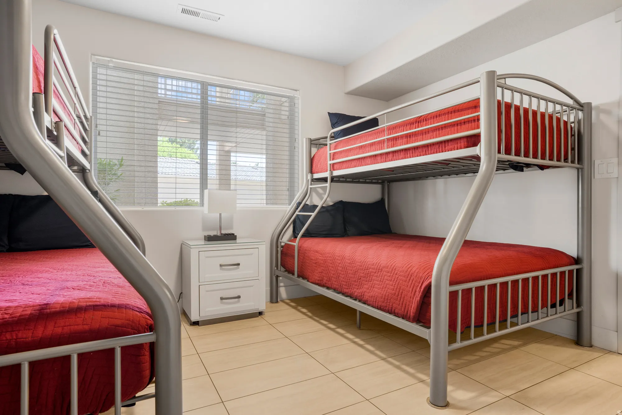 Room featuring two metal bunk bed frames, a window with horizontal blinds, and ceramic tile flooring