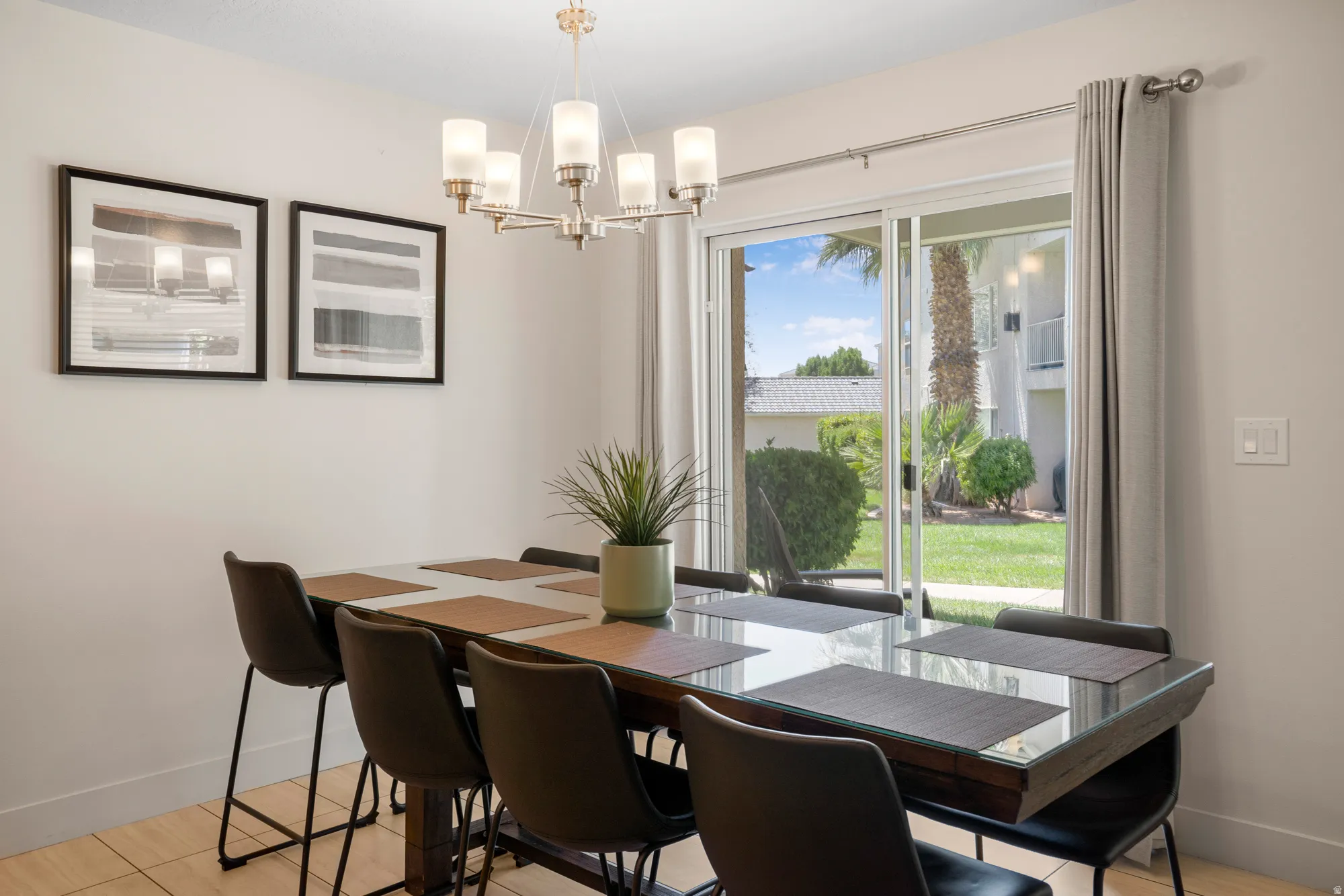 Dining area featuring wood-finish flooring, a modern chandelier with frosted glass shades, and sliding glass doors opening to a green space