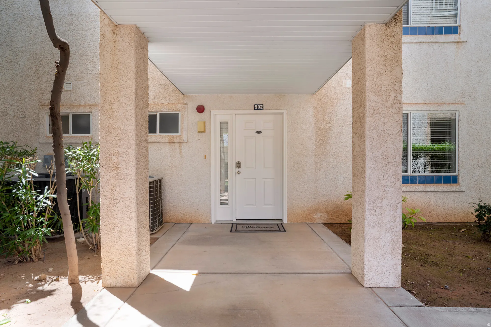 Covered entrance featuring a white paneled door with a sidelight, textured exterior walls, and a concrete walkway