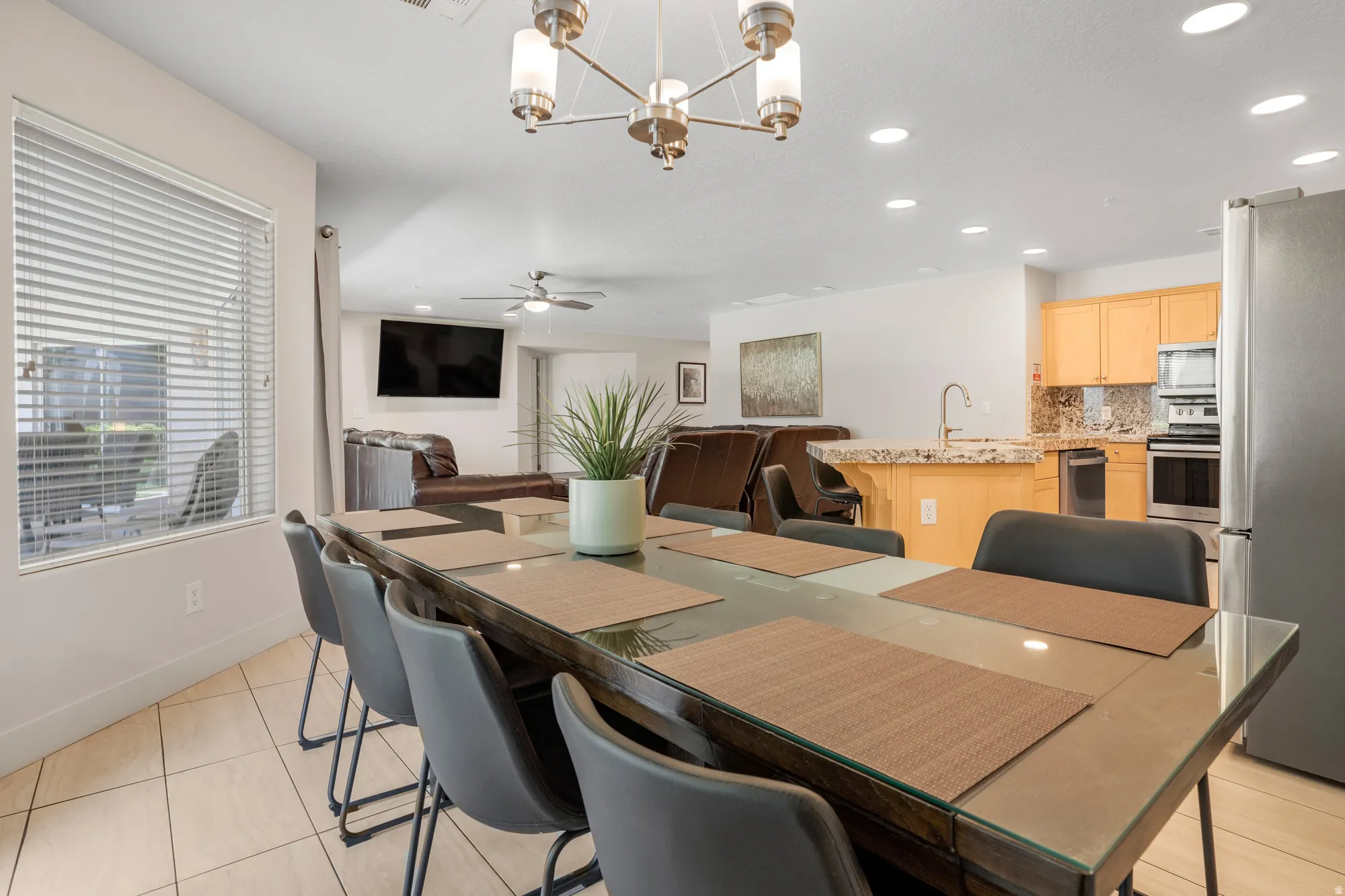 Open-concept living area featuring a dining space with tile flooring, a kitchen with light wood cabinetry and granite-finish countertops, stainless steel appliances, and recessed lighting throughout