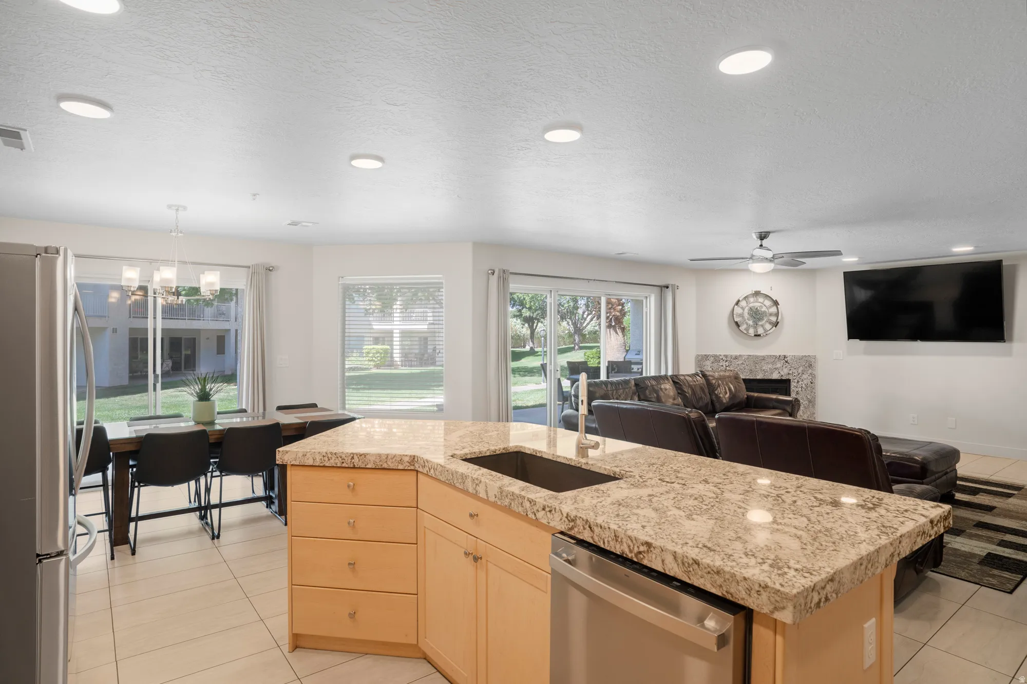Open-concept living space with a kitchen island featuring a stainless steel sink and dishwasher, light-toned cabinetry, and granite-style countertops