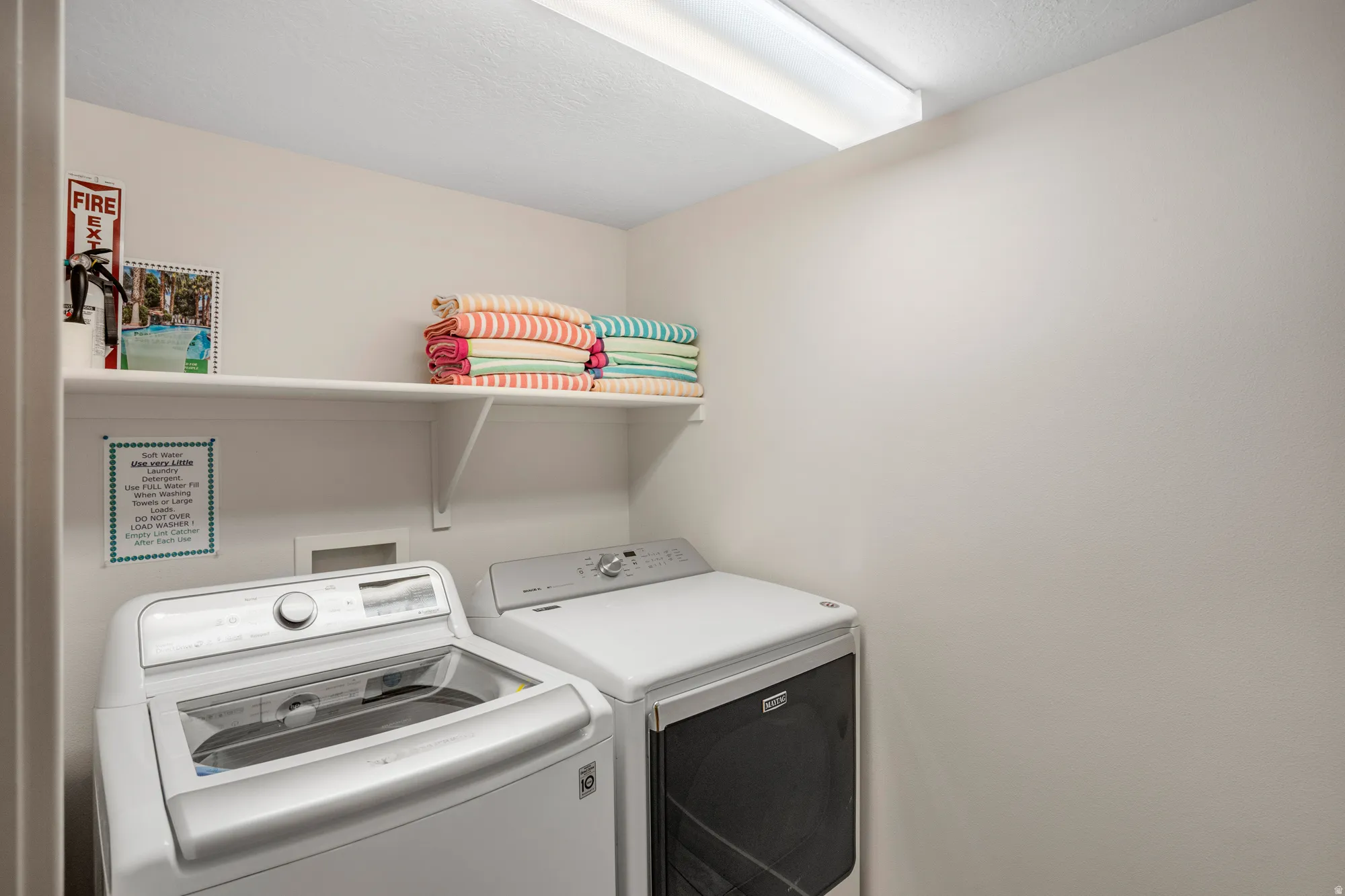 Dedicated laundry area featuring a top-load washing machine, front-load dryer, and overhead shelving for storage