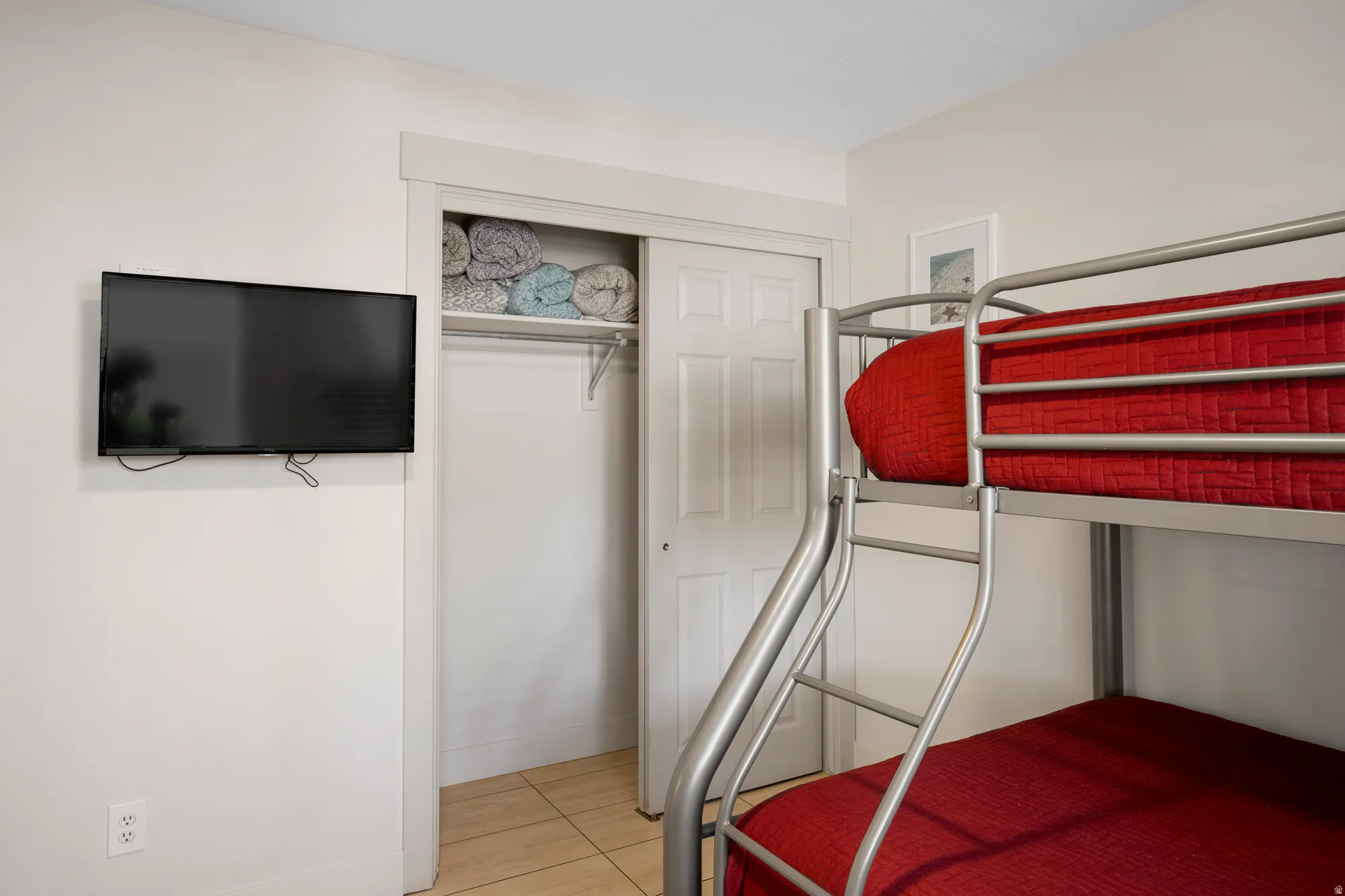 Room featuring a built-in metal bunk bed, wall-mounted television, and a closet with bifold doors