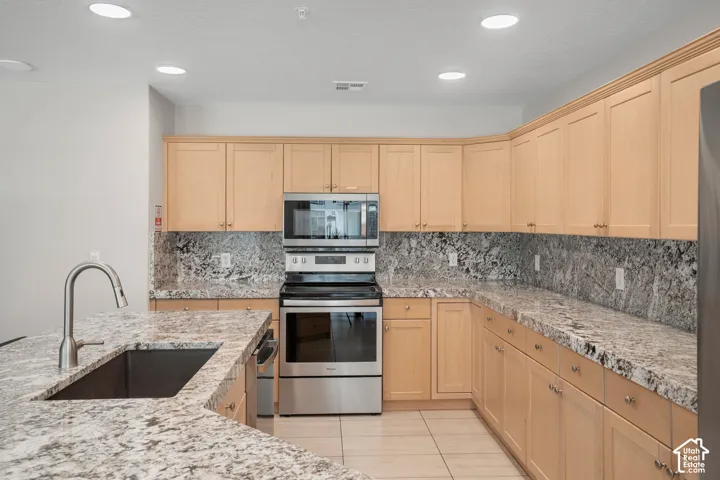 Spacious kitchen featuring light wood cabinetry, stone countertops, a stainless steel sink with a gooseneck faucet, and integrated stainless steel appliances