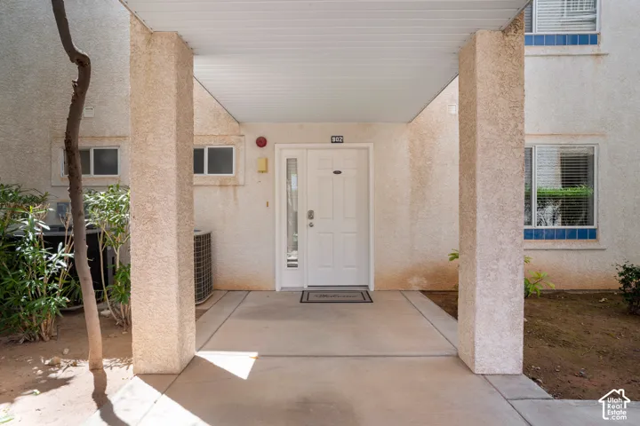 Covered entrance featuring a white paneled door with a sidelight, textured exterior walls, and a concrete walkway