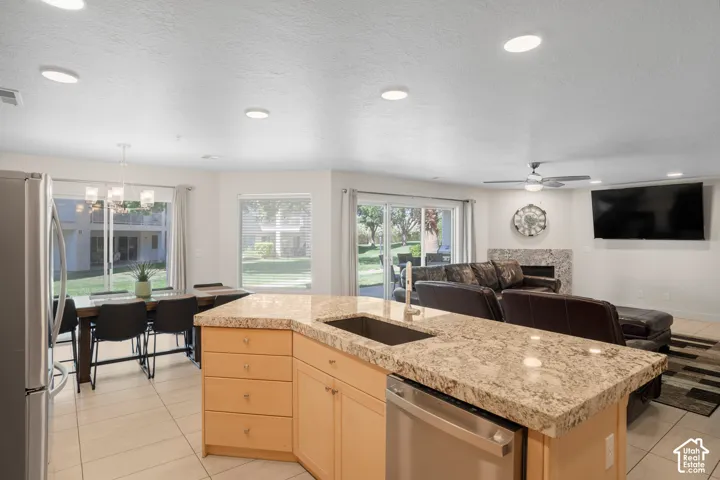 Open-concept living space with a kitchen island featuring a stainless steel sink and dishwasher, light-toned cabinetry, and granite-style countertops