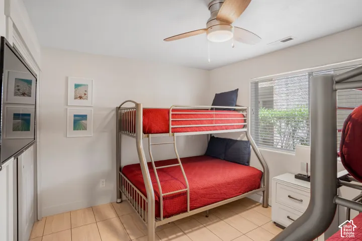 Room featuring metal bunk beds, tile flooring, and a ceiling fan with light fixture