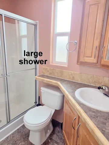 Bathroom featuring a spacious glass-enclosed shower, a vanity with wood-finish cabinetry, a white basin sink, and a textured countertop with a backsplash