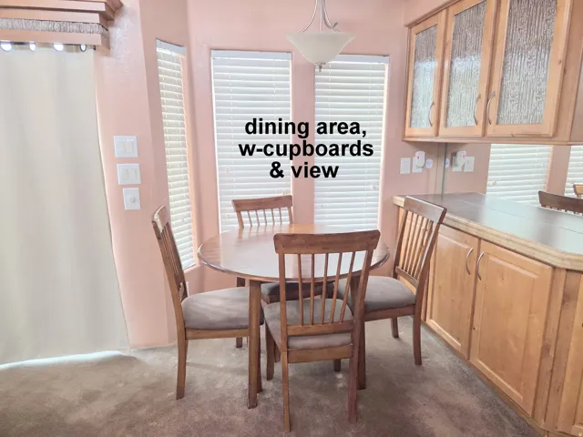 Dining area featuring three large windows with blinds, a built-in light wood cabinetry unit with upper glass-fronted cabinets, and a coordinating wood-finish countertop
