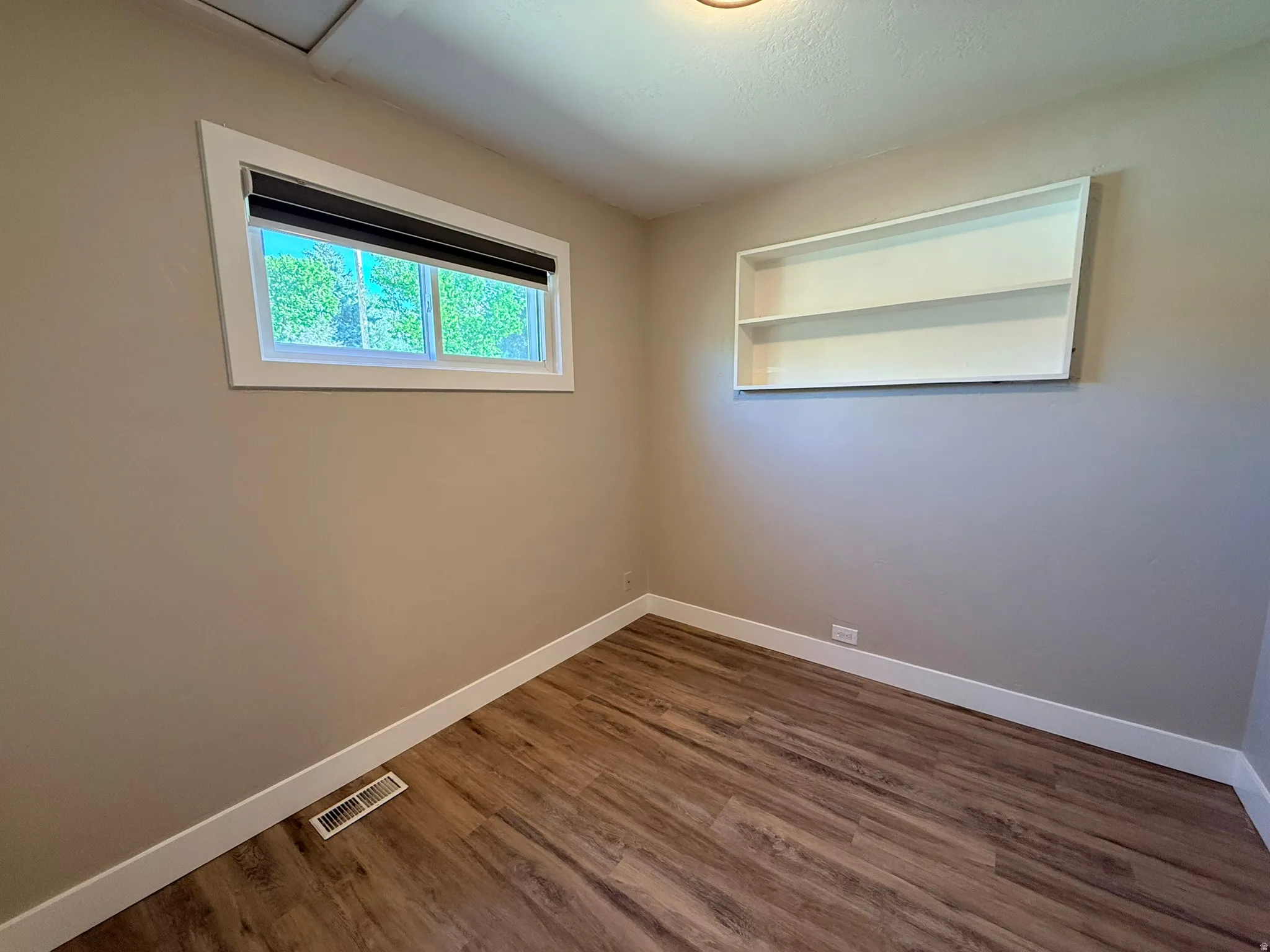 Wood-finish flooring, built-in shelving, white trim, and a window with a roller shade