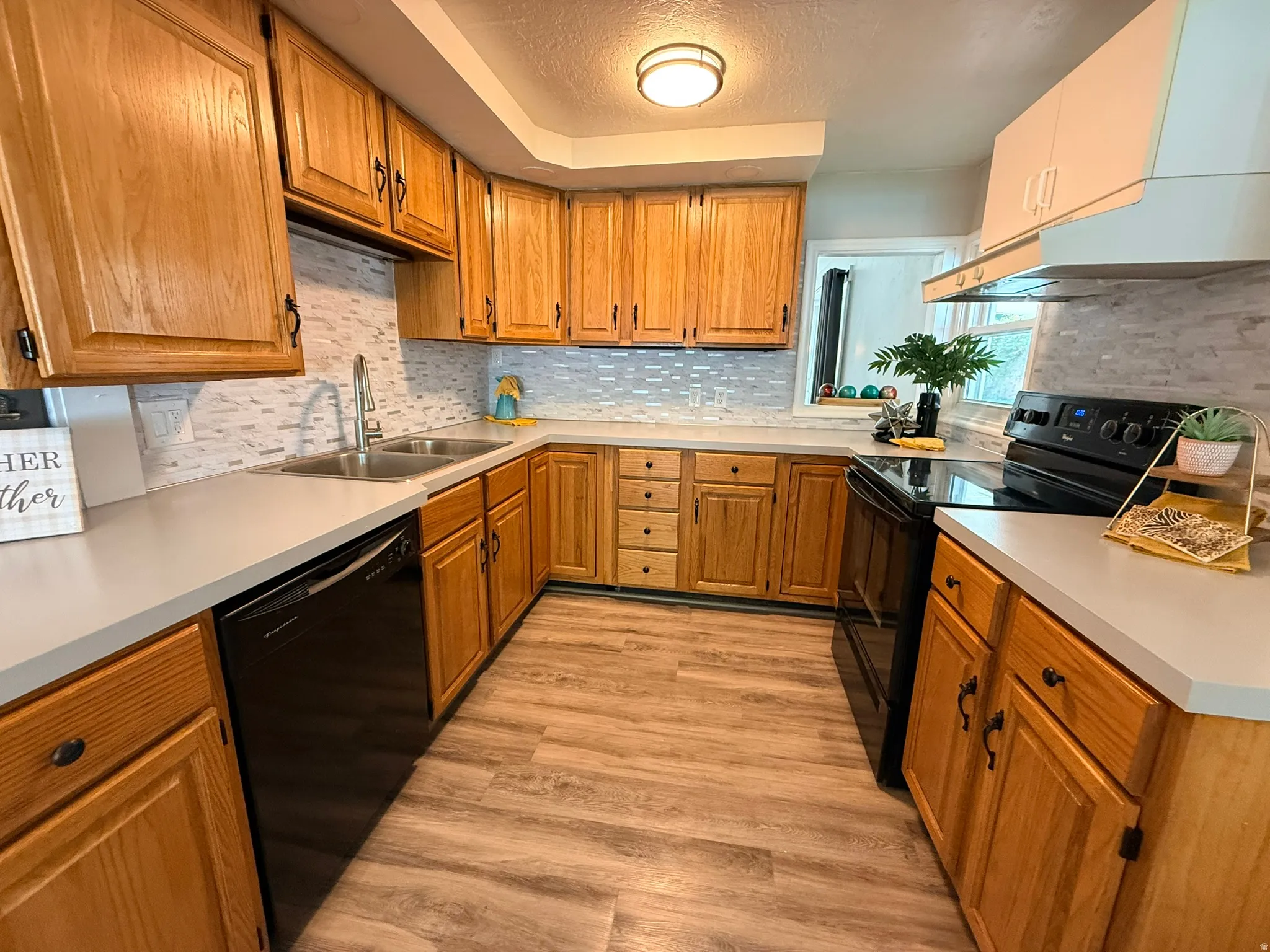 U-shaped kitchen featuring wood cabinetry, light-toned countertops, a tile backsplash, and wood-finish flooring