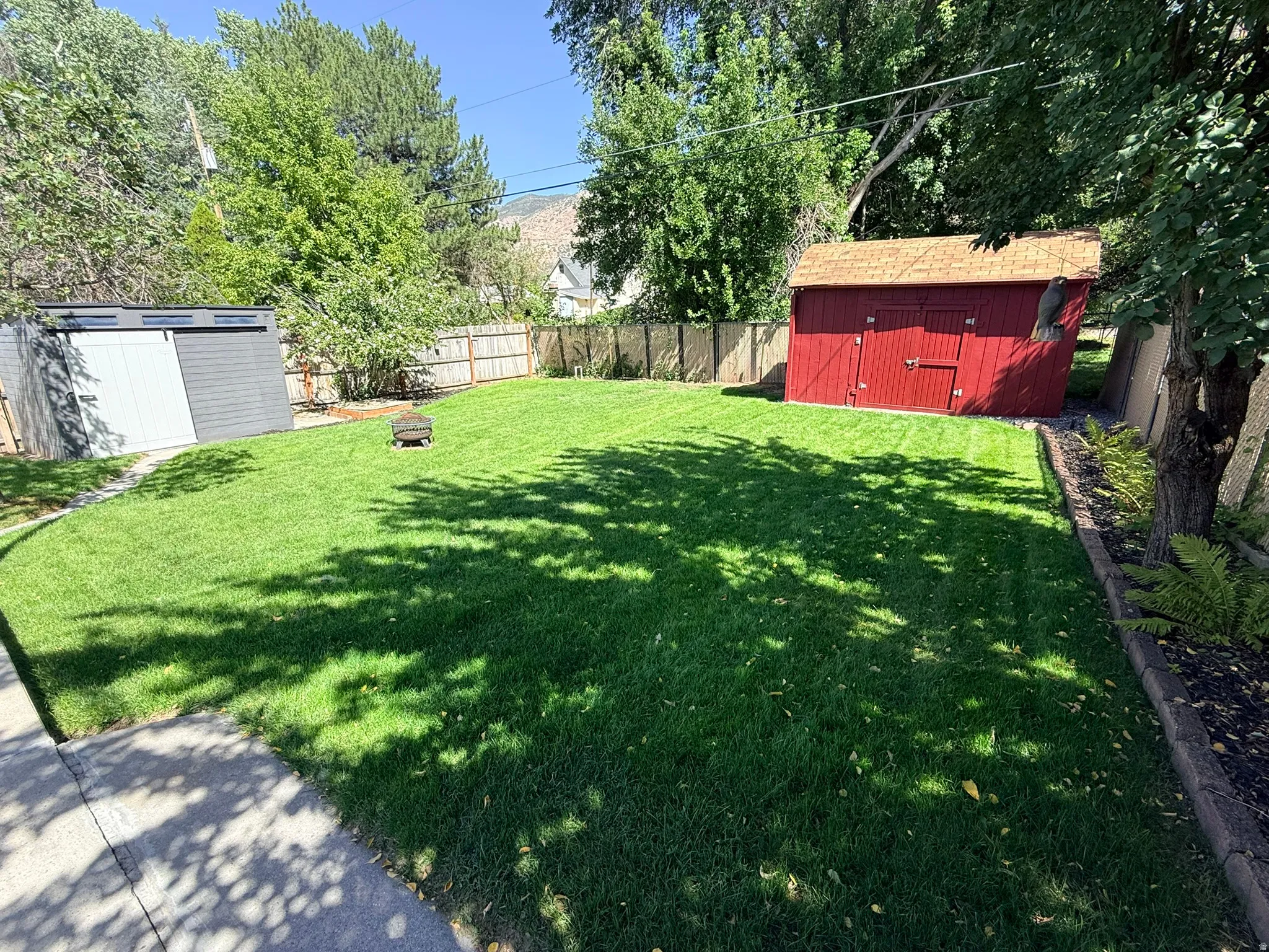 Expansive lawn bordered by a wood fence, featuring a red storage shed with a shingle roof and a gray storage shed with a white sliding door