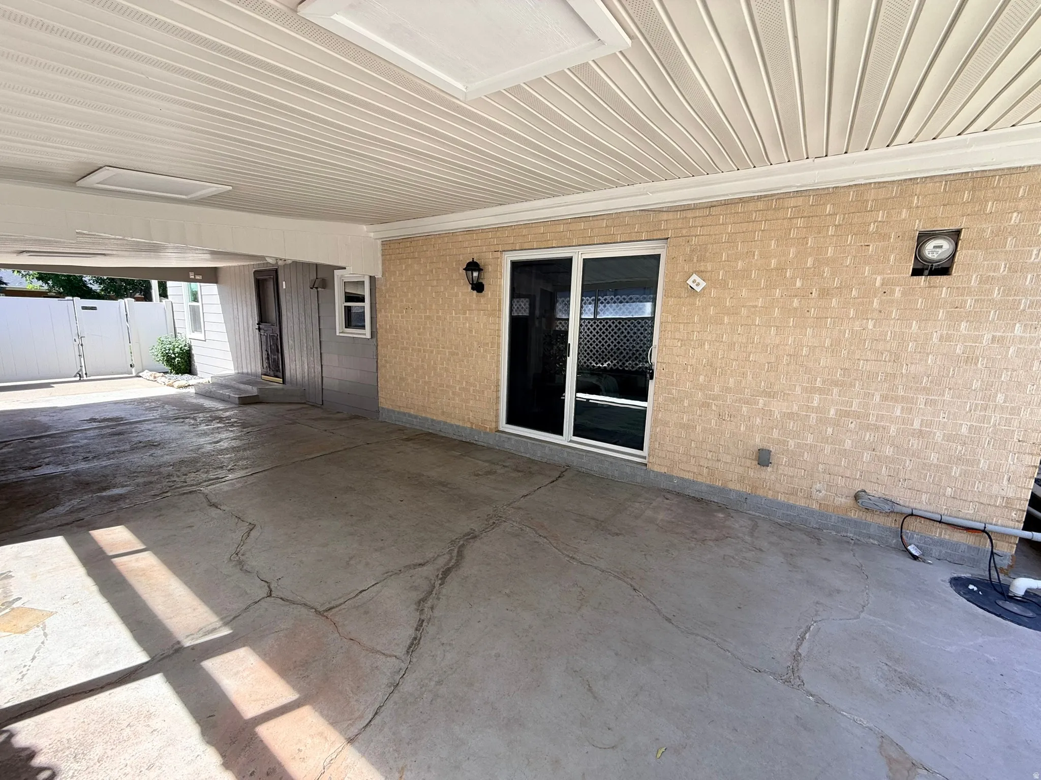 Covered outdoor area featuring a textured concrete floor, brick exterior wall, and white vinyl soffit ceiling with recessed lighting