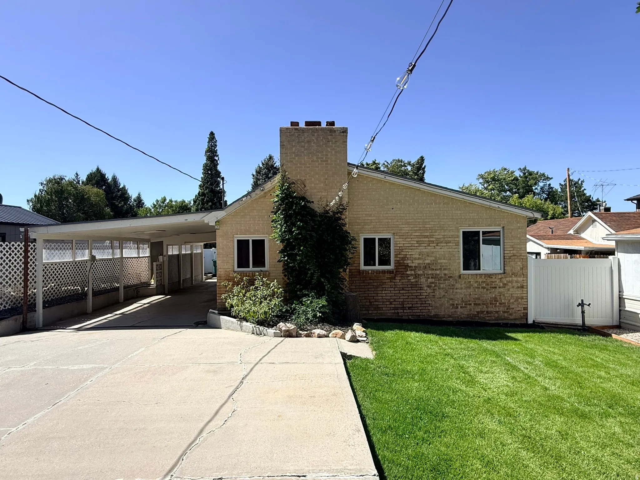 Brick exterior with a prominent chimney, concrete driveway, attached carport, and a manicured lawn