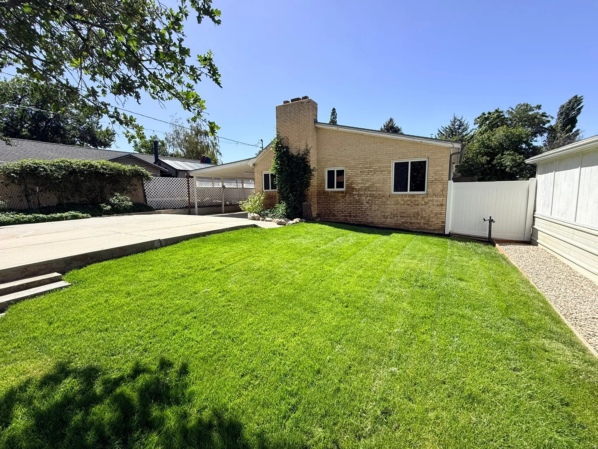 Expansive lawn area with a concrete driveway and a covered carport