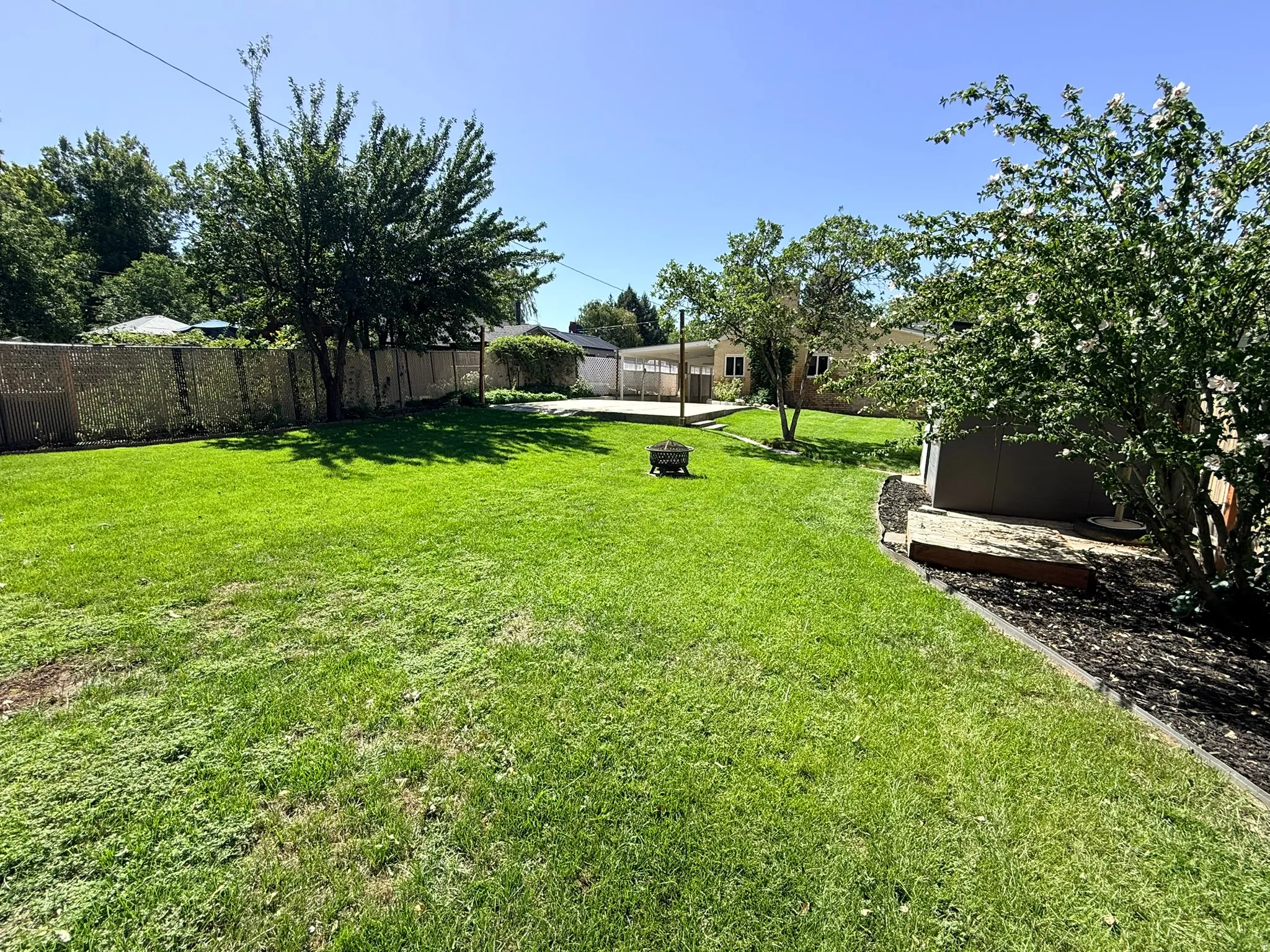 Expansive backyard featuring a lush lawn, mature trees, and a privacy fence