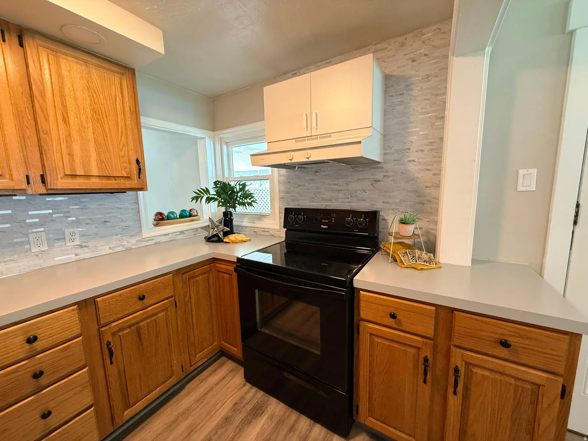 Laminate wood-finish flooring, light gray countertops, white rectangular tile backsplash, and wood cabinetry with black hardware