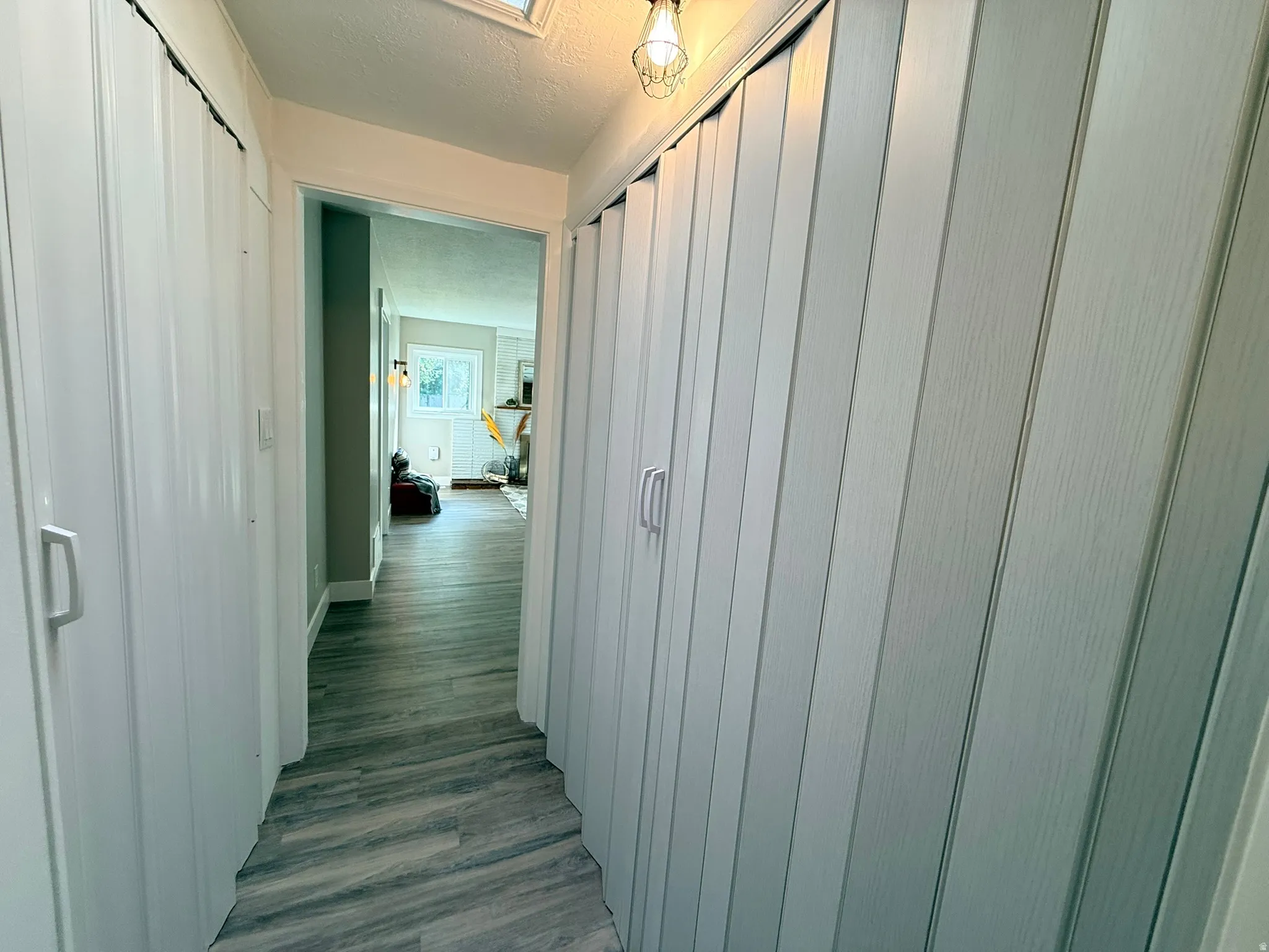 Hallway featuring wood-finish flooring, two accordion-style closet doors, a ceiling-mounted light fixture, and a skylight