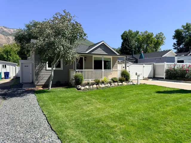 Manicured front lawn, white picket railing on the porch, landscaped garden bed, gravel driveway, and a white privacy fence
