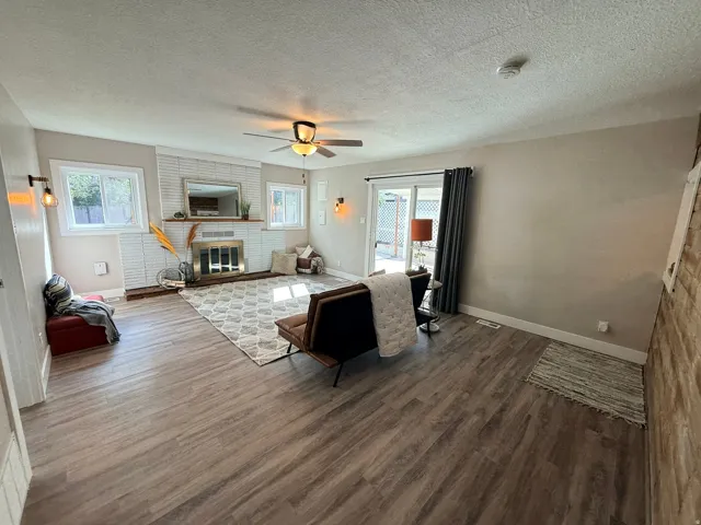 Wood-finish flooring throughout, featuring a white brick fireplace with a brass insert, and multiple windows