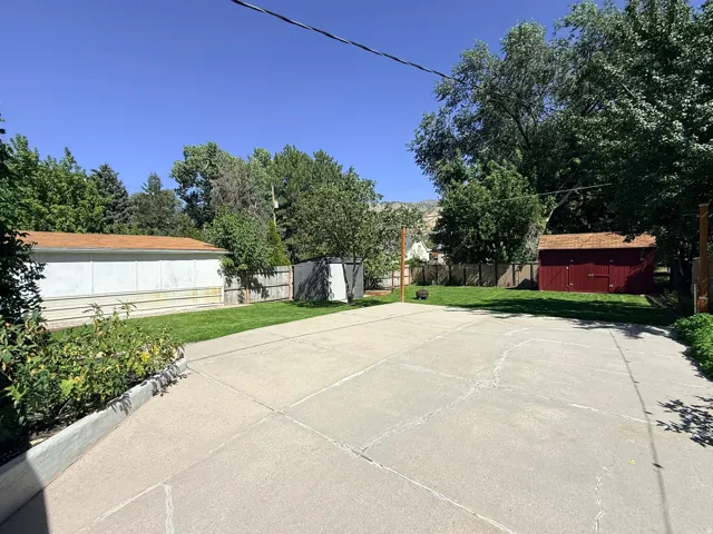 Spacious concrete pad, expansive grassy area, mature trees, wood fence, and a red storage shed with a shingled roof
