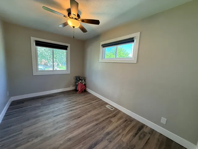 Wood-finish flooring, white trim, two windows, and a ceiling fan with integrated lighting