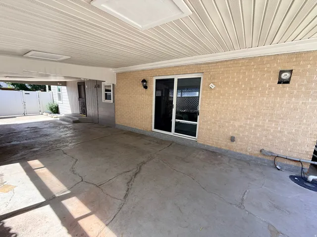 Covered outdoor area featuring a textured concrete floor, brick exterior wall, and white vinyl soffit ceiling with recessed lighting