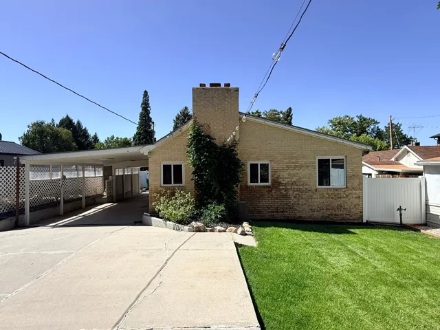 Brick exterior with a prominent chimney, concrete driveway, attached carport, and a manicured lawn