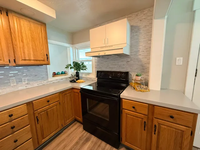 Laminate wood-finish flooring, light gray countertops, white rectangular tile backsplash, and wood cabinetry with black hardware