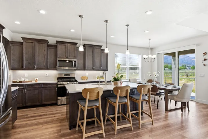 Open-concept kitchen with wood-finish flooring, dark wood cabinetry, white countertops, stainless steel appliances, and a central island with pendant lighting