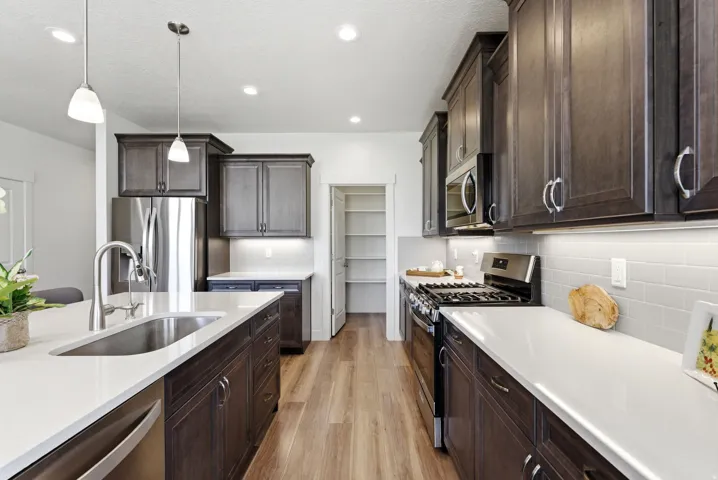 Contemporary kitchen featuring dark wood cabinetry, light countertops, stainless steel appliances, and wood-finish flooring