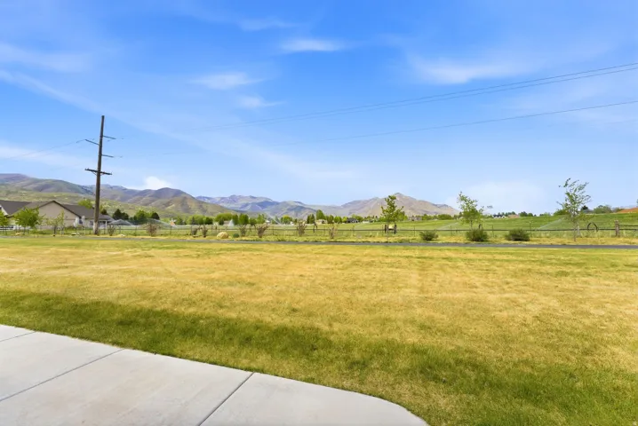 Expansive green space with distant mountain scenery, featuring a paved pathway and partial residential structures