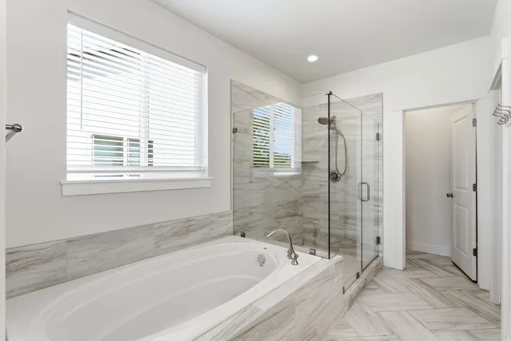 Spacious bathroom featuring a built-in soaking tub, a frameless glass shower enclosure with a built-in niche, floor-to-ceiling tile in the shower, large format tile surrounding the tub, and herringbone pattern tile flooring