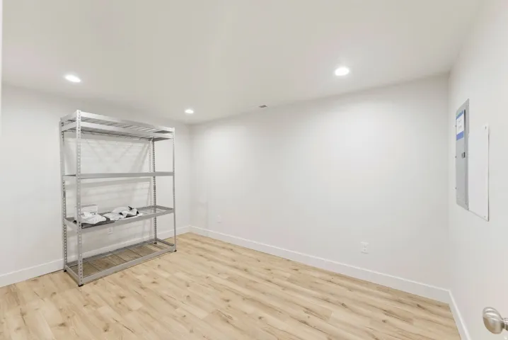 Spacious room featuring wood-finish flooring, white baseboards, recessed lighting, and a neutral color palette