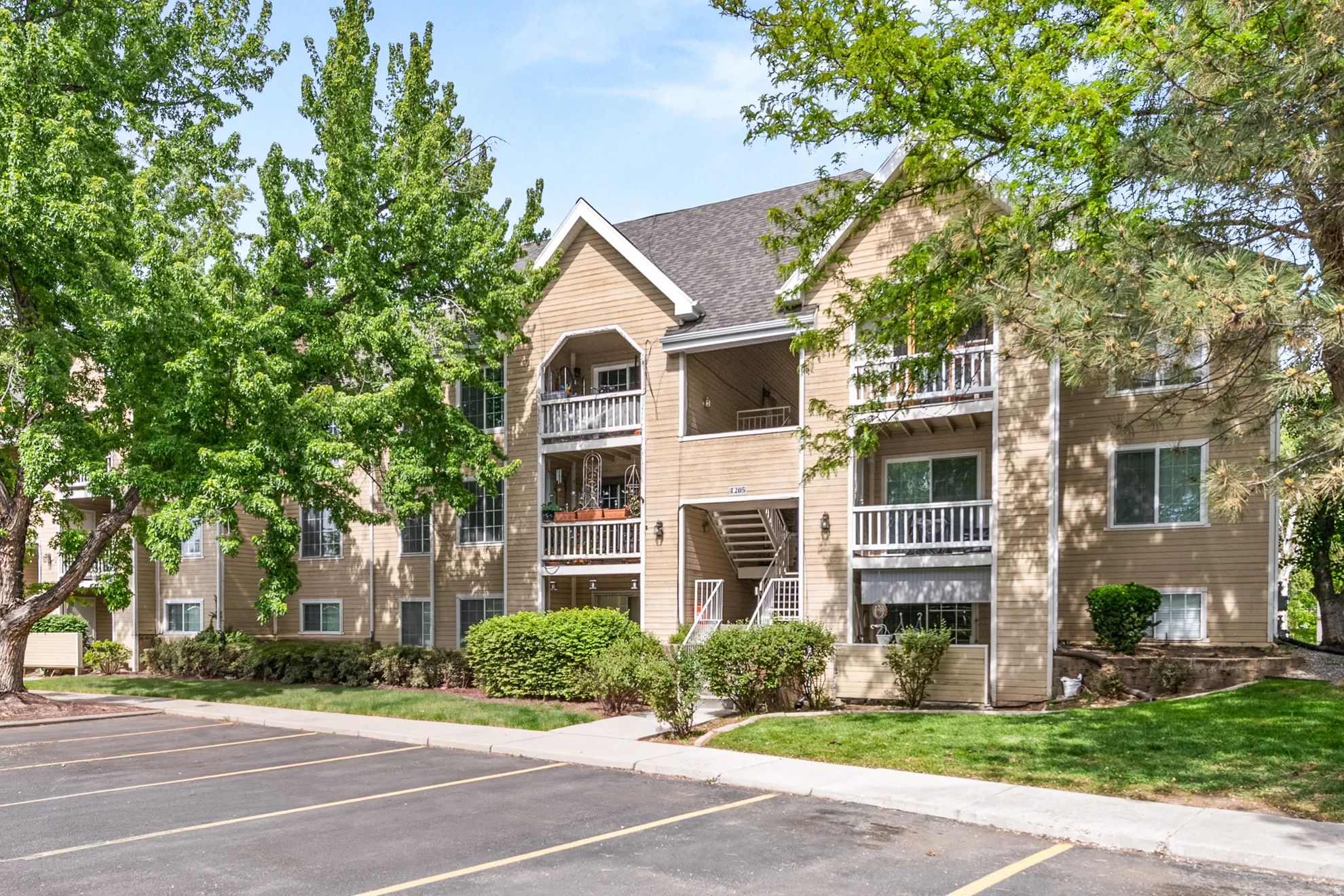 Multi-story residential building featuring balconies, tan siding, and a dark shingle roof