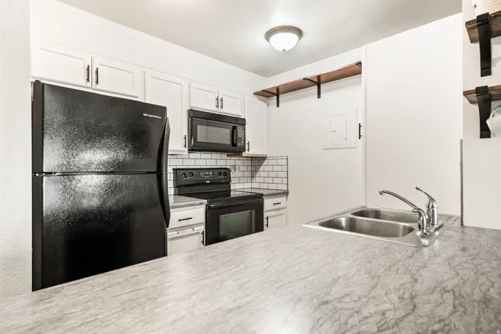 Kitchen featuring white cabinetry with black hardware, subway tile backsplash, and dark appliances