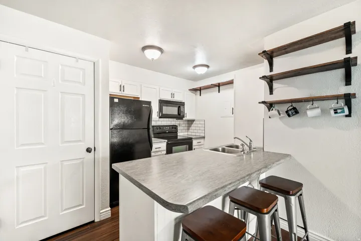 Kitchen featuring a breakfast bar with a stone-finish countertop, dual-basin stainless steel sink, white cabinetry with black hardware, and wood-finish flooring