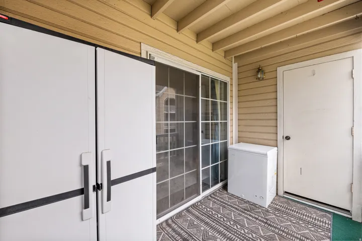 Outdoor patio featuring an overhead beam structure, sliding glass door with screen, and a storage closet