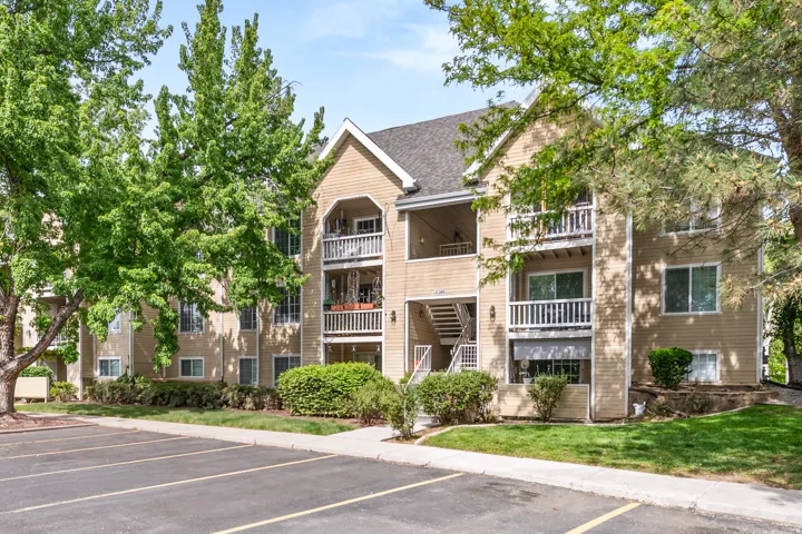 Multi-story residential building featuring balconies, tan siding, and a dark shingle roof