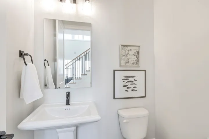 Pedestal sink with a matte black faucet, rectangular mirror, and overhead vanity lighting
