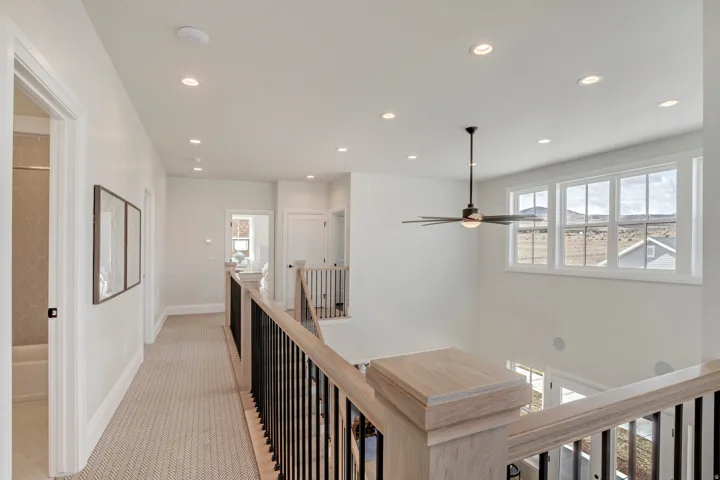 Upper level landing featuring light-toned wood railings with black metal balusters, recessed lighting, and a contemporary ceiling fan