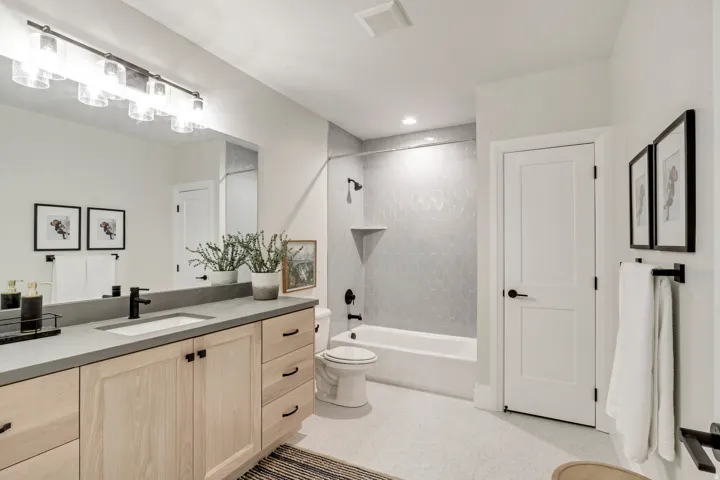 Modern bathroom featuring a single vanity with light wood cabinetry, a built-in sink, and a dark countertop