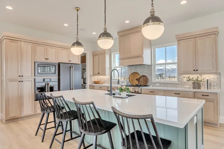 Spacious kitchen featuring a large island with seating, light wood-finish cabinetry, integrated stainless steel appliances, and a decorative tile backsplash