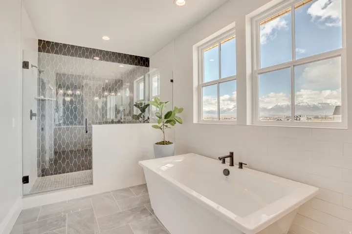Spacious bathroom featuring a freestanding soaking tub with matte black fixtures, a walk-in shower with glass enclosure and patterned tile, and large windows with mountain scenery