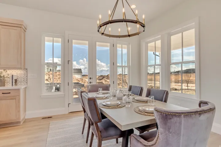 Dining area featuring a contemporary chandelier, multiple large windows, French patio doors, wood-finish flooring, and light-toned cabinetry with a patterned backsplash