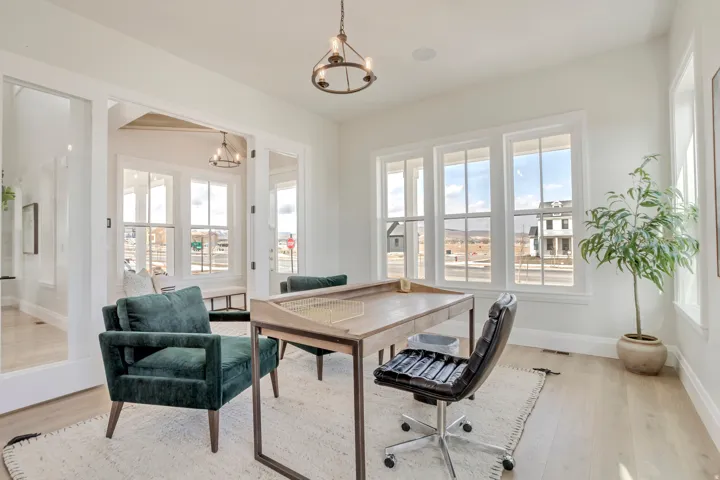 Dedicated office space featuring expansive windows, light wood-finish flooring, white trim, and a contemporary chandelier