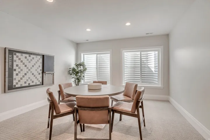 Recessed lighting illuminates a spacious room featuring a neutral color palette, two large egress windows, and chevron-patterned carpeting
