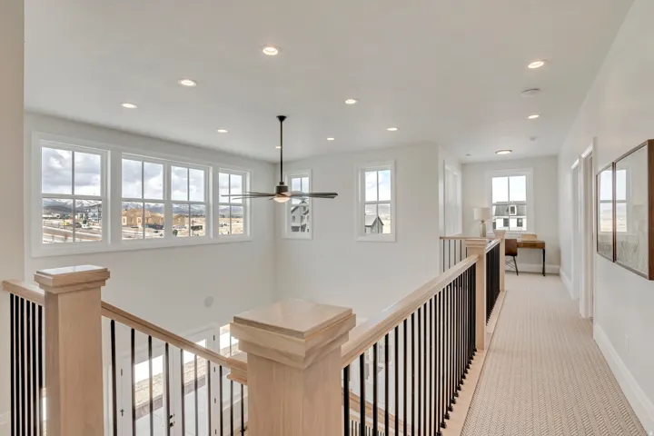 Upper-level landing featuring a series of rectangular windows, a ceiling fan with light, recessed lighting, and light wood-finish railings with black metal spindles