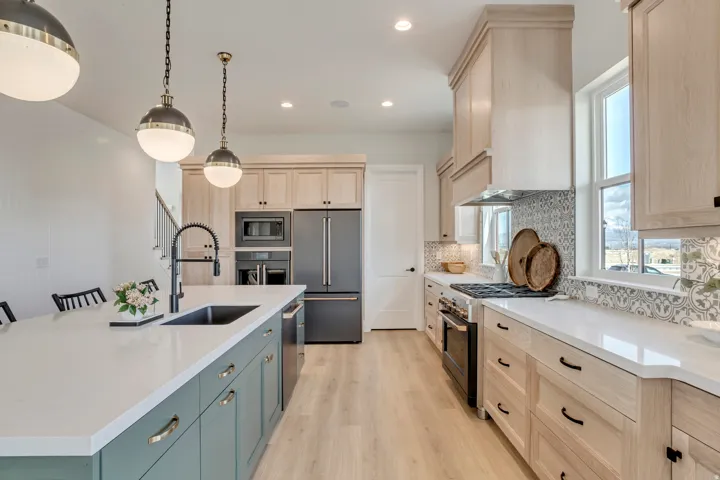 Bright kitchen featuring a substantial island with a basin sink and matte black faucet, light wood-finish flooring, light wood cabinetry, white countertops, and patterned tile backsplash